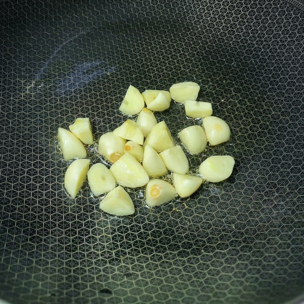 Spicchi daglio che friggono in un wok con olio caldo.