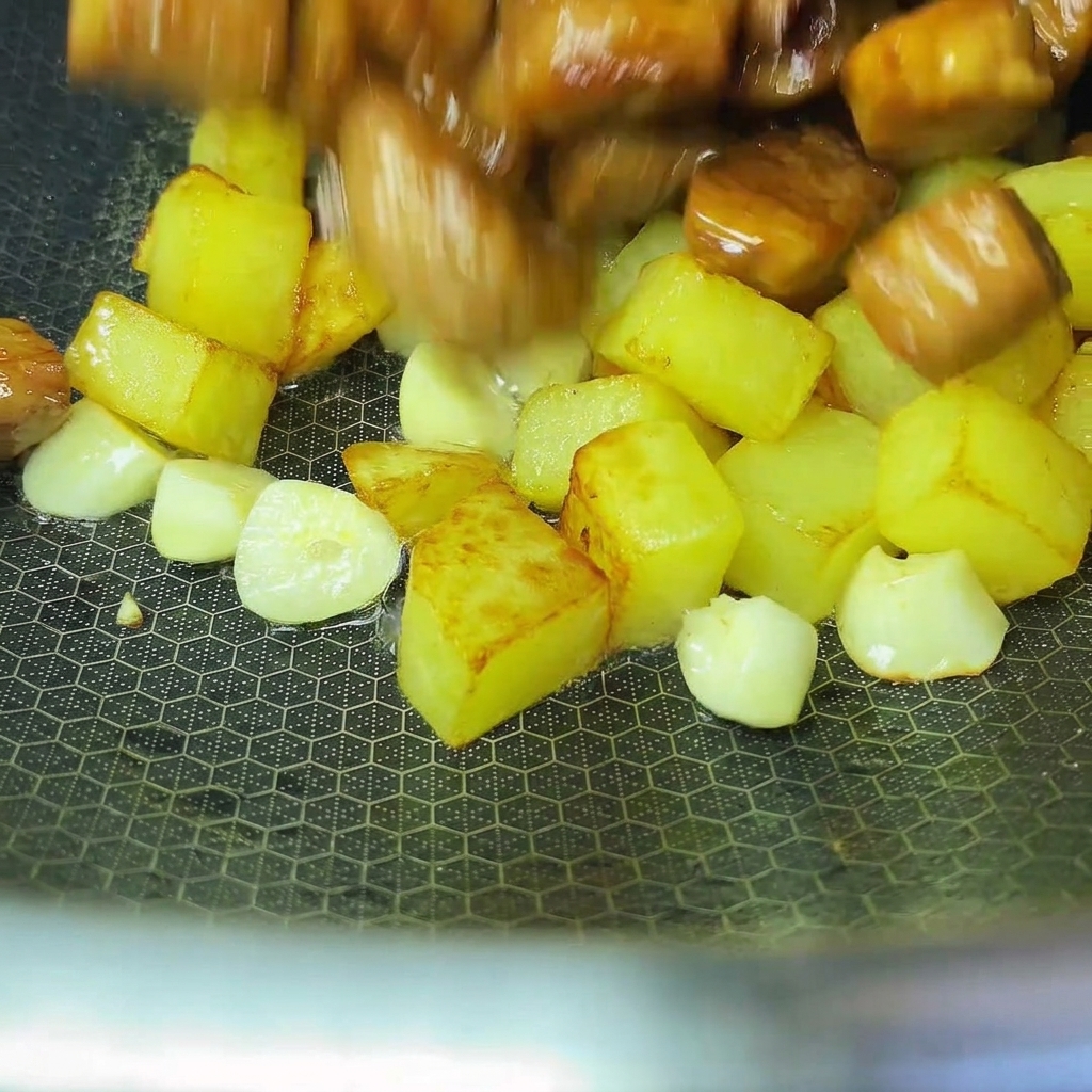 Patate e maiale cotti che vengono uniti insieme in un wok.