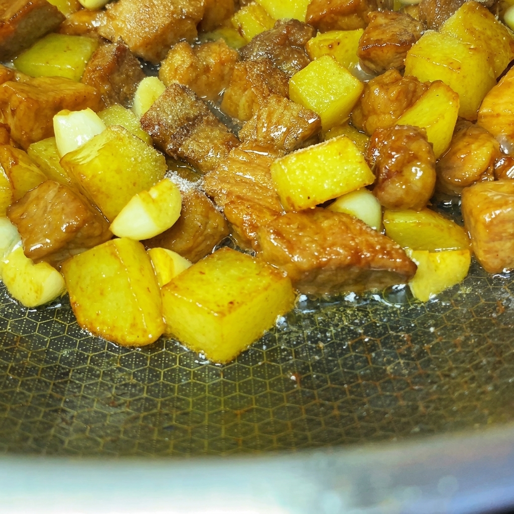 Spezie e semi di sesamo cosparsi uniformemente sui cubetti di maiale e patate saltati.