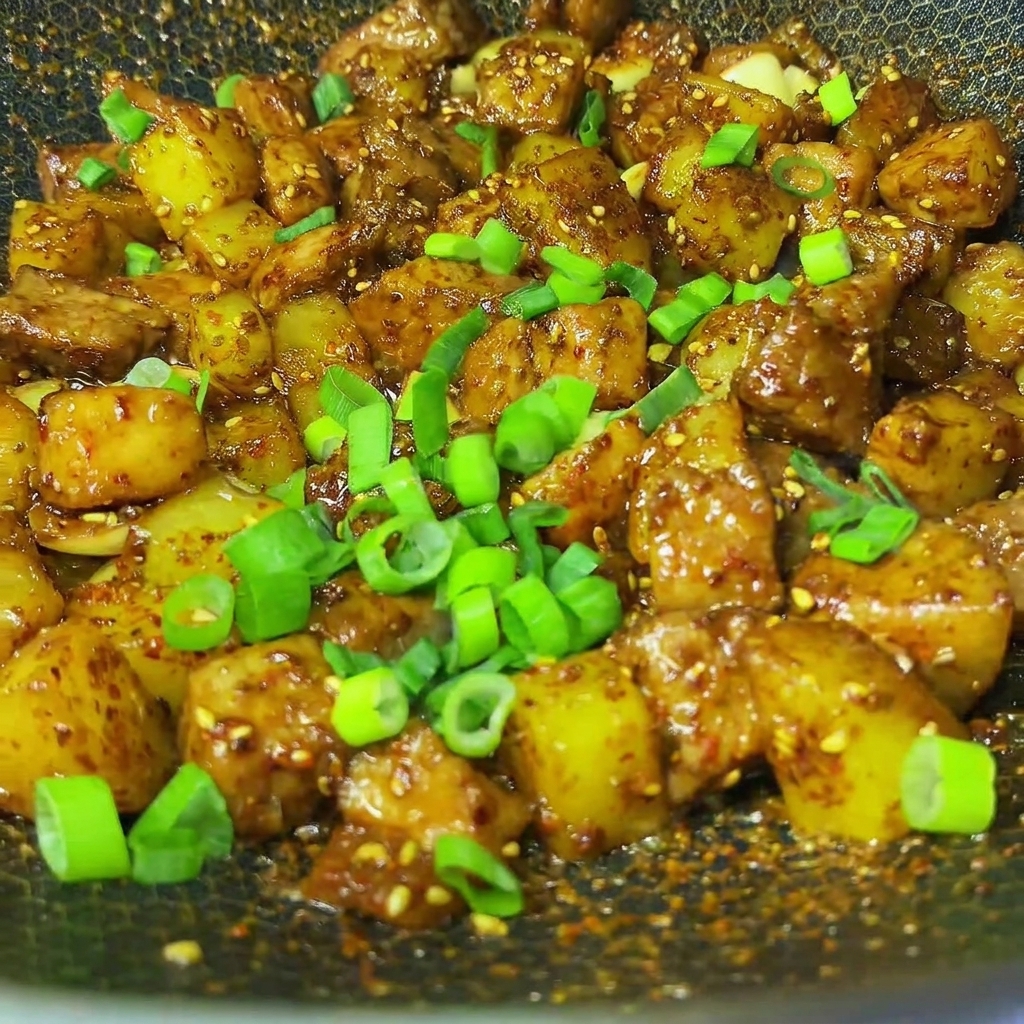 Cipollotti freschi tritati cosparsi sul maiale e patate al cumino barbecue finito in un wok.