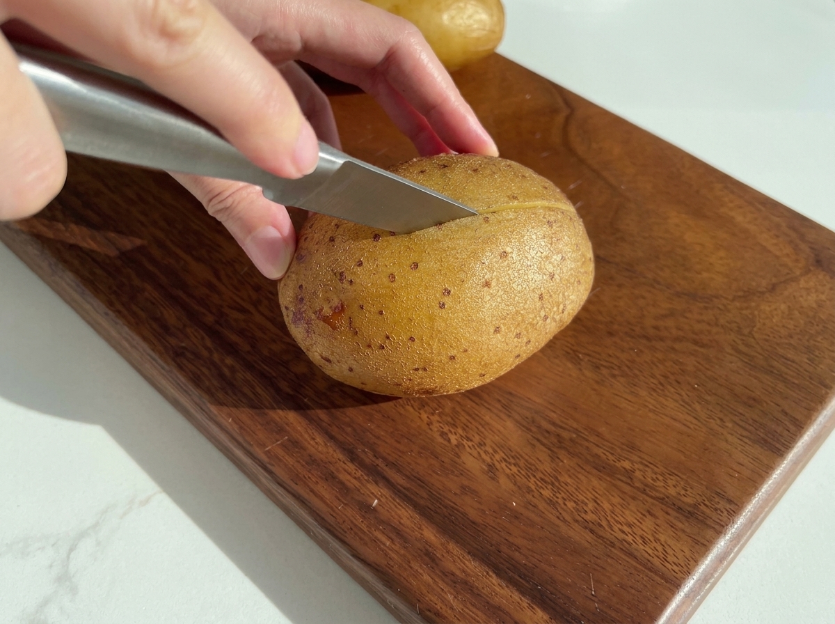 Un coltello che taglia a metà una patata cotta su un tagliere di legno.