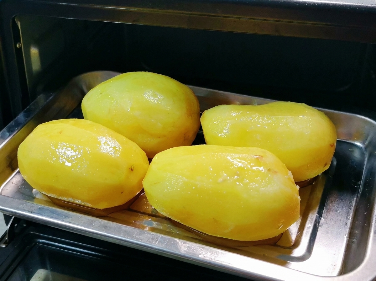 Una teglia di metallo con patate intere oliate inserita allinterno di un piccolo forno nero.