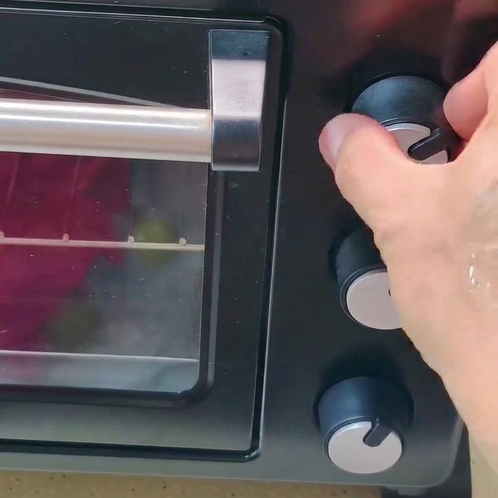 Una mano che gira la manopola di controllo della temperatura su un forno nero.