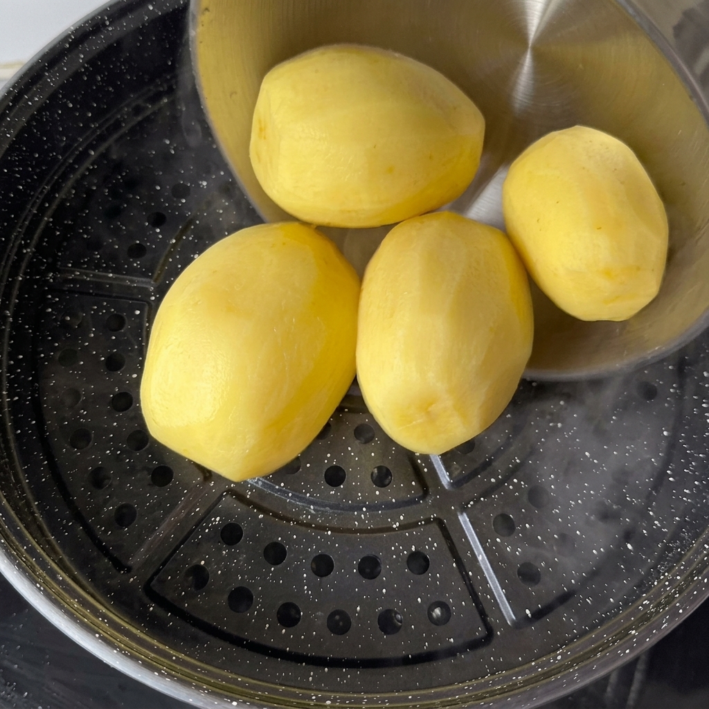 Patate a pasta gialla pelate disposte su un cestello per la cottura al vapore sopra acqua bollente.