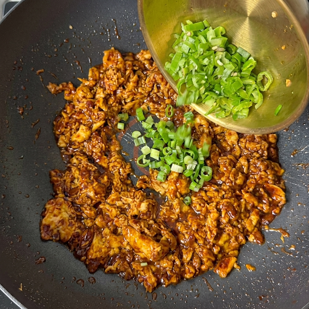 Cipollotti tritati e pezzi di peperone verde versati da una ciotola dorata sul composto di uova cotte.
