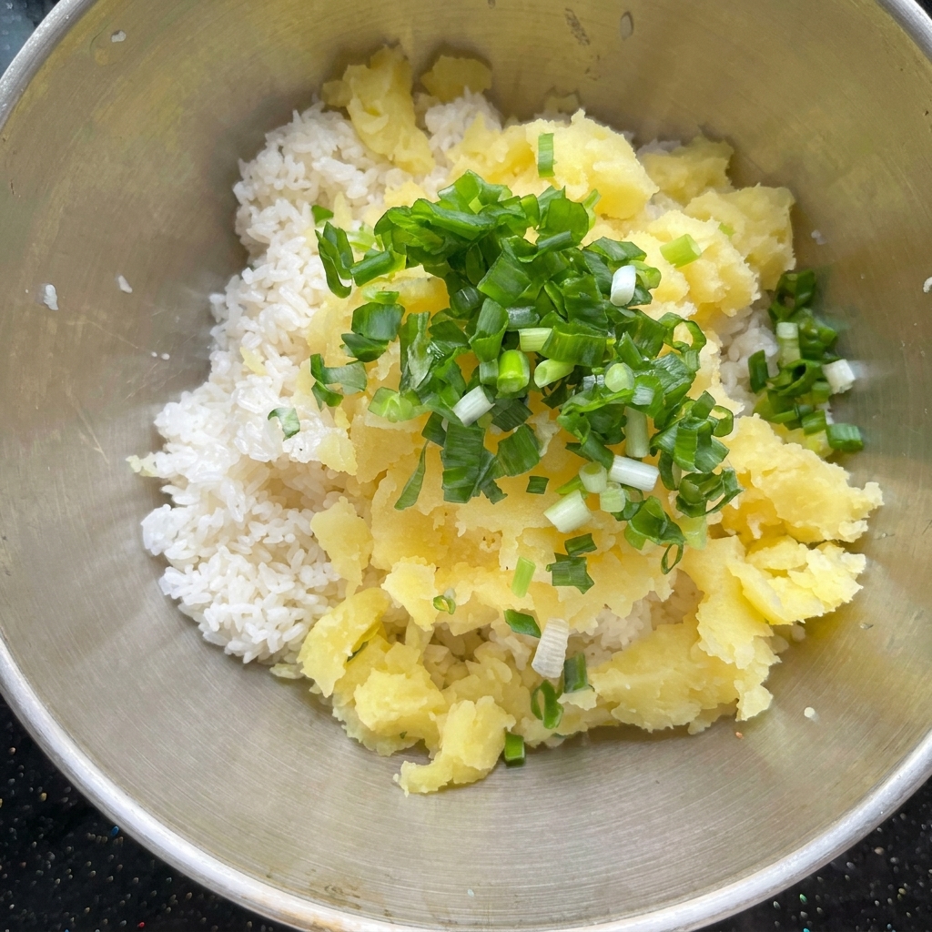 Pezzi di patata cotta e condimenti combinati con il riso cotto in una ciotola di metallo.
