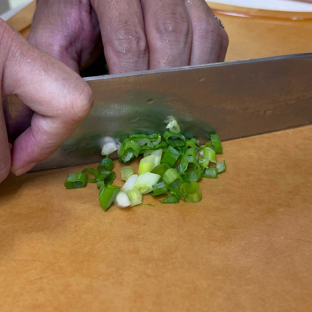 Cipollotti tagliati a rondelle con un coltello su un tagliere.