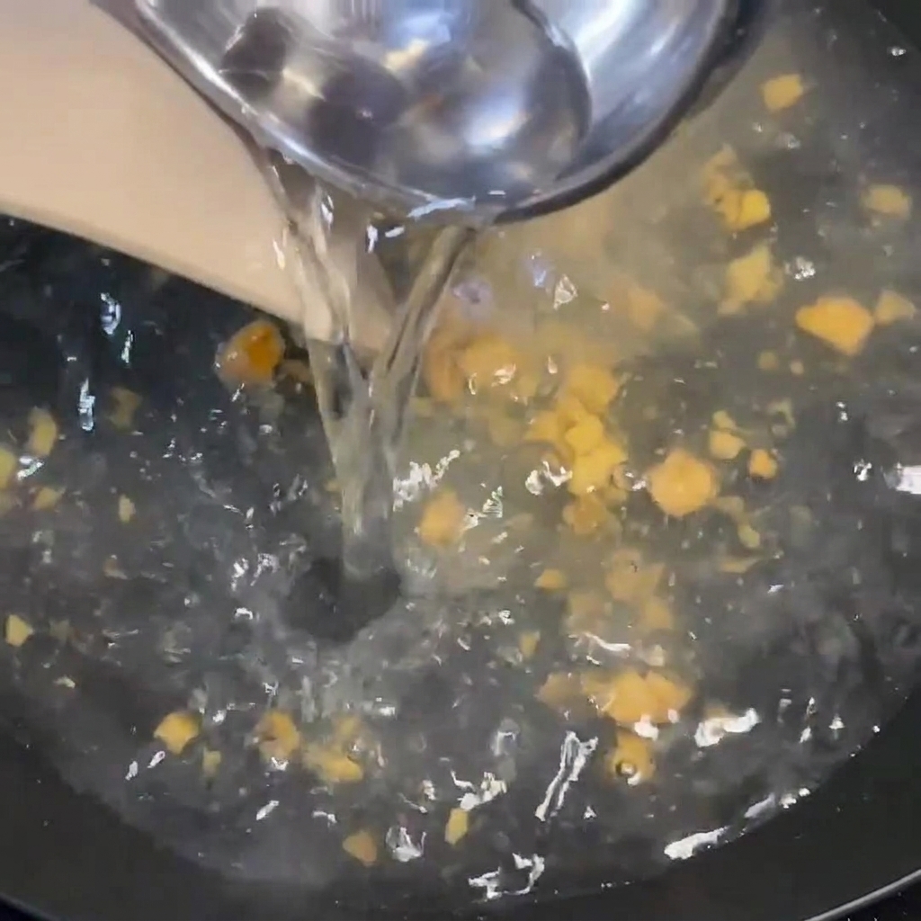 Acqua calda versata da un mestolo in una pentola bollente contenente condimento e pezzi di zenzero.