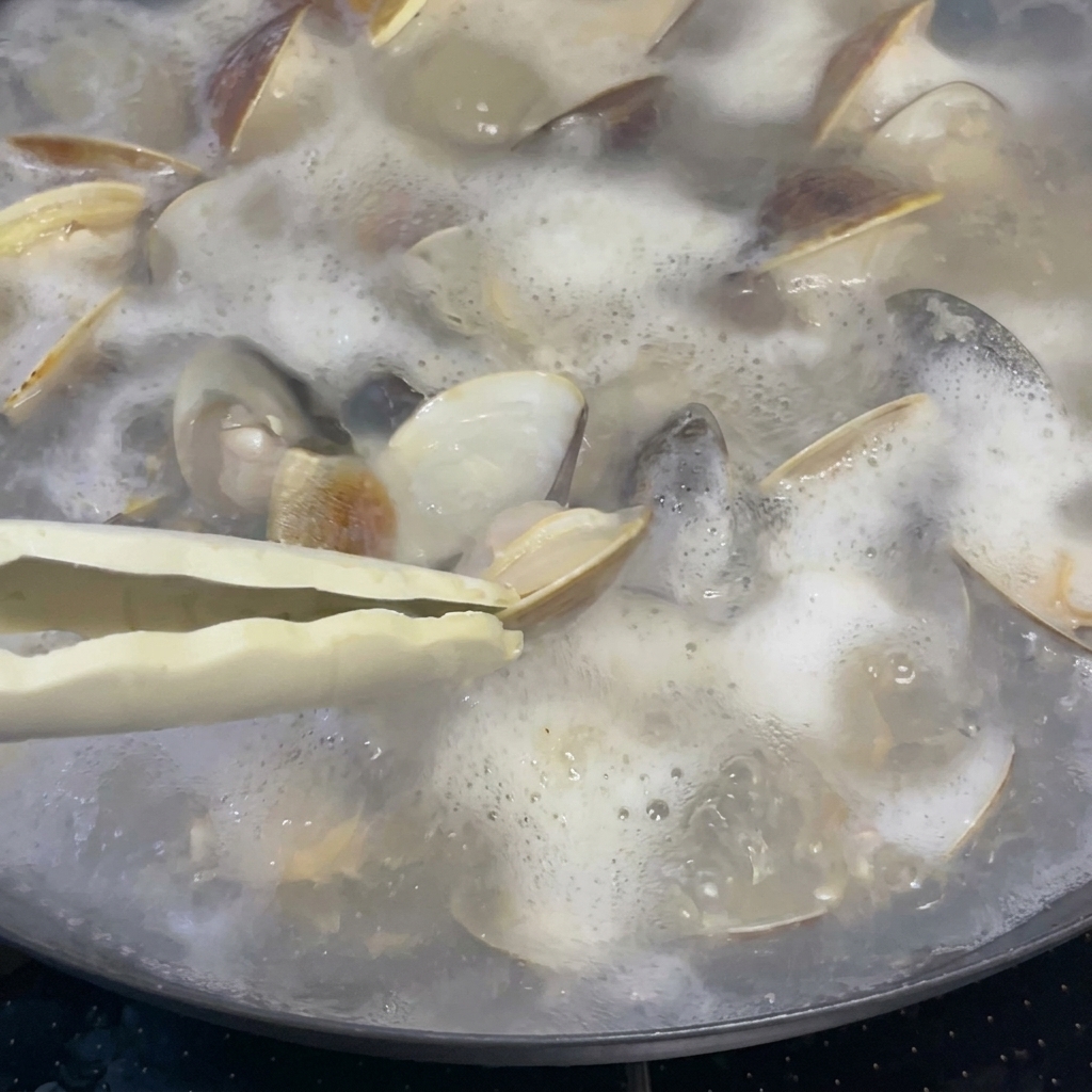 Un cucchiaio di vino di riso versato in una pentola di vongole e brodo che sobbollono.