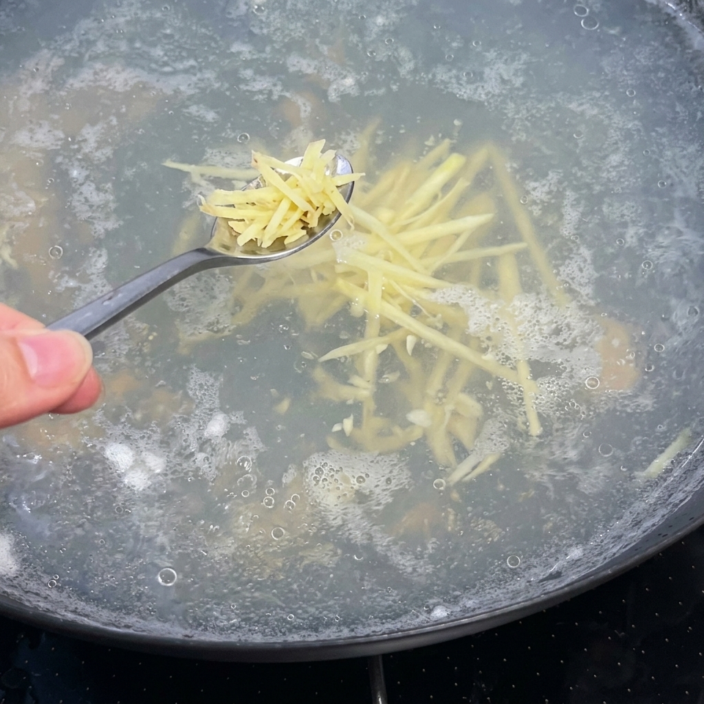 Un cucchiaio di zenzero a julienne aggiunto in una pentola bollente di brodo limpido.
