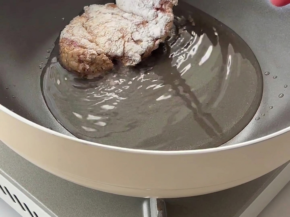 Una coscia di pollo ricoperta di amido di mais inserita in una padella con olio da cucina caldo.