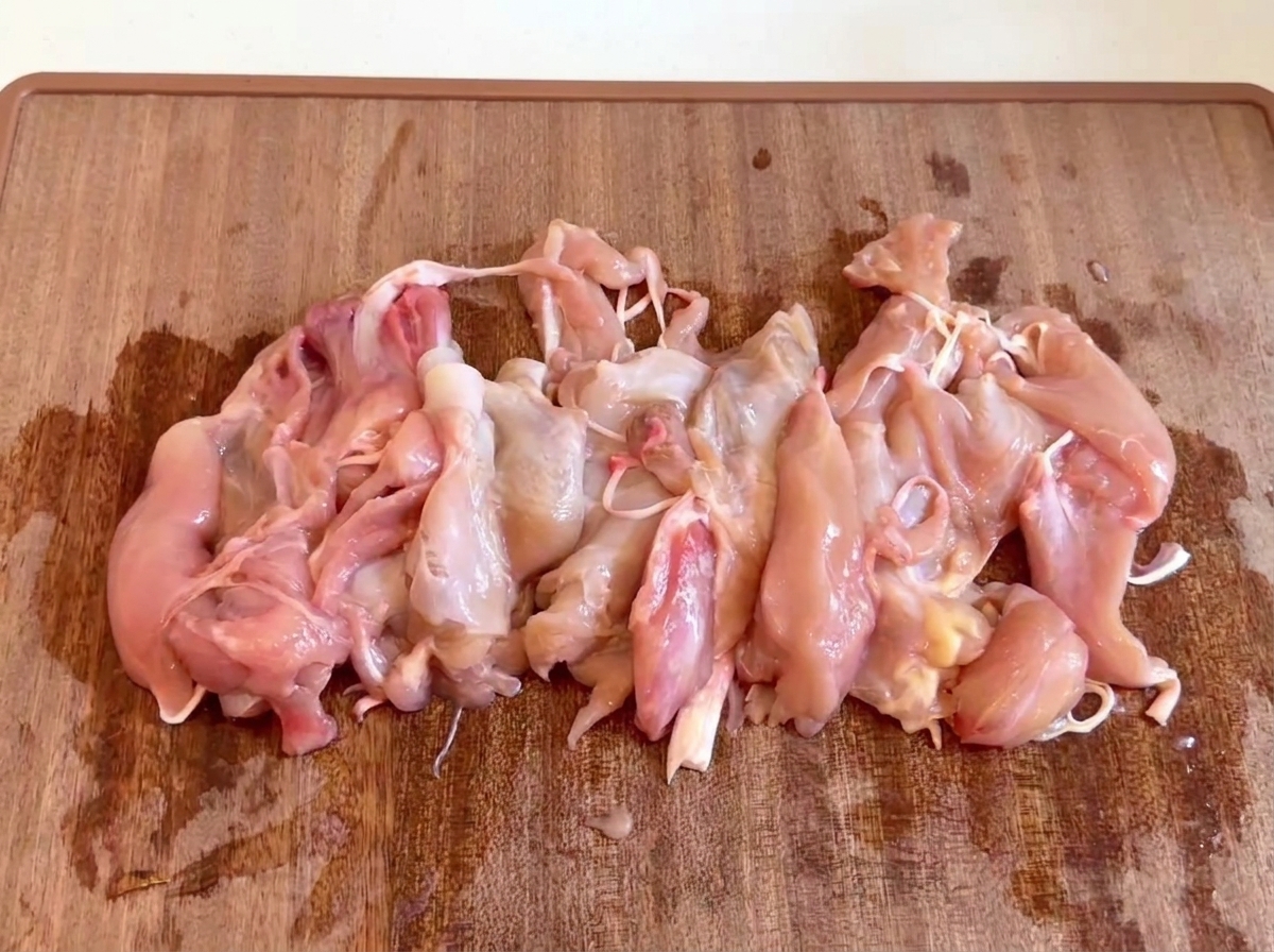 Pezzi di carne di pollo cruda e disossata riuniti insieme su un tagliere di legno.