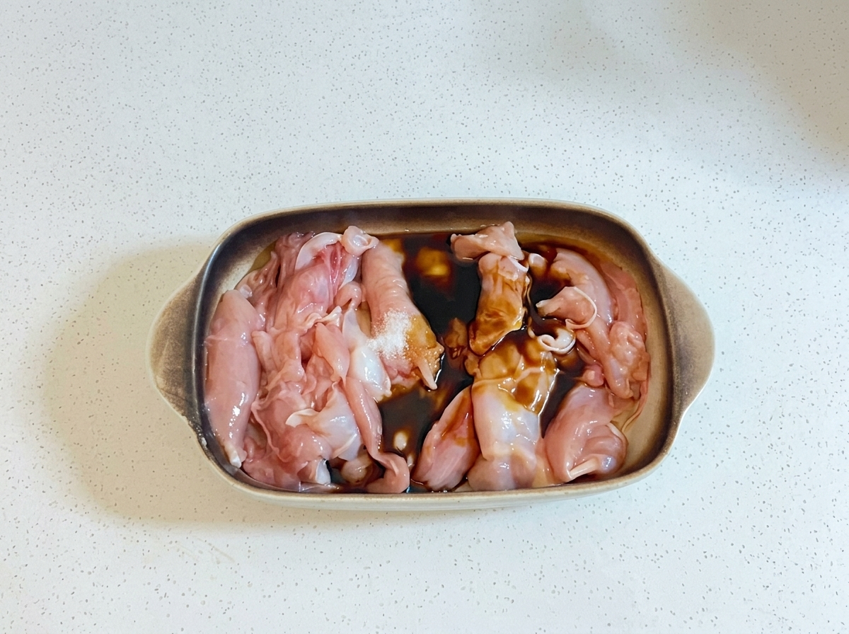 Liquidi di cottura scuri e olio versati sui pezzi di pollo crudi in una teglia.