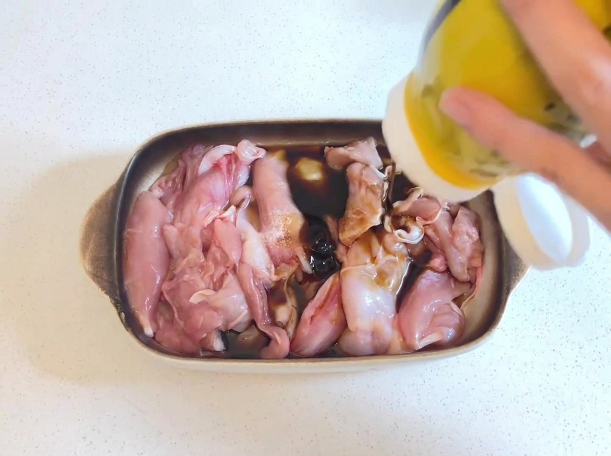 Salsa di ostriche densa e scura spremuta da una bottiglia gialla sui pezzi di pollo crudi immersi in una marinata di salsa di soia.