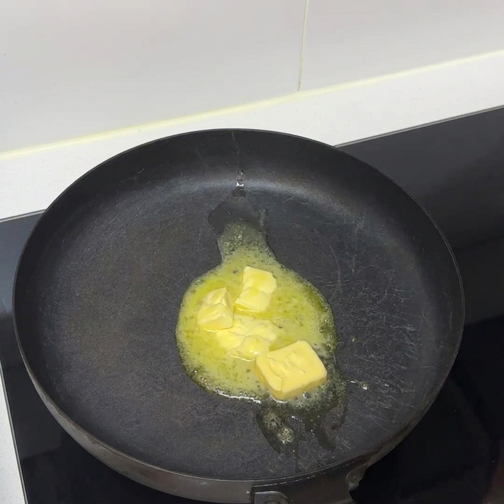 Pezzi di burro che si sciolgono in liquido in una padella scura su un piano cottura.
