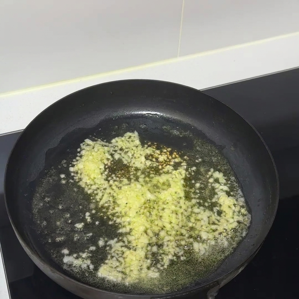 Aglio tritato e burro fuso che sfrigolano insieme in una padella antiaderente nera.