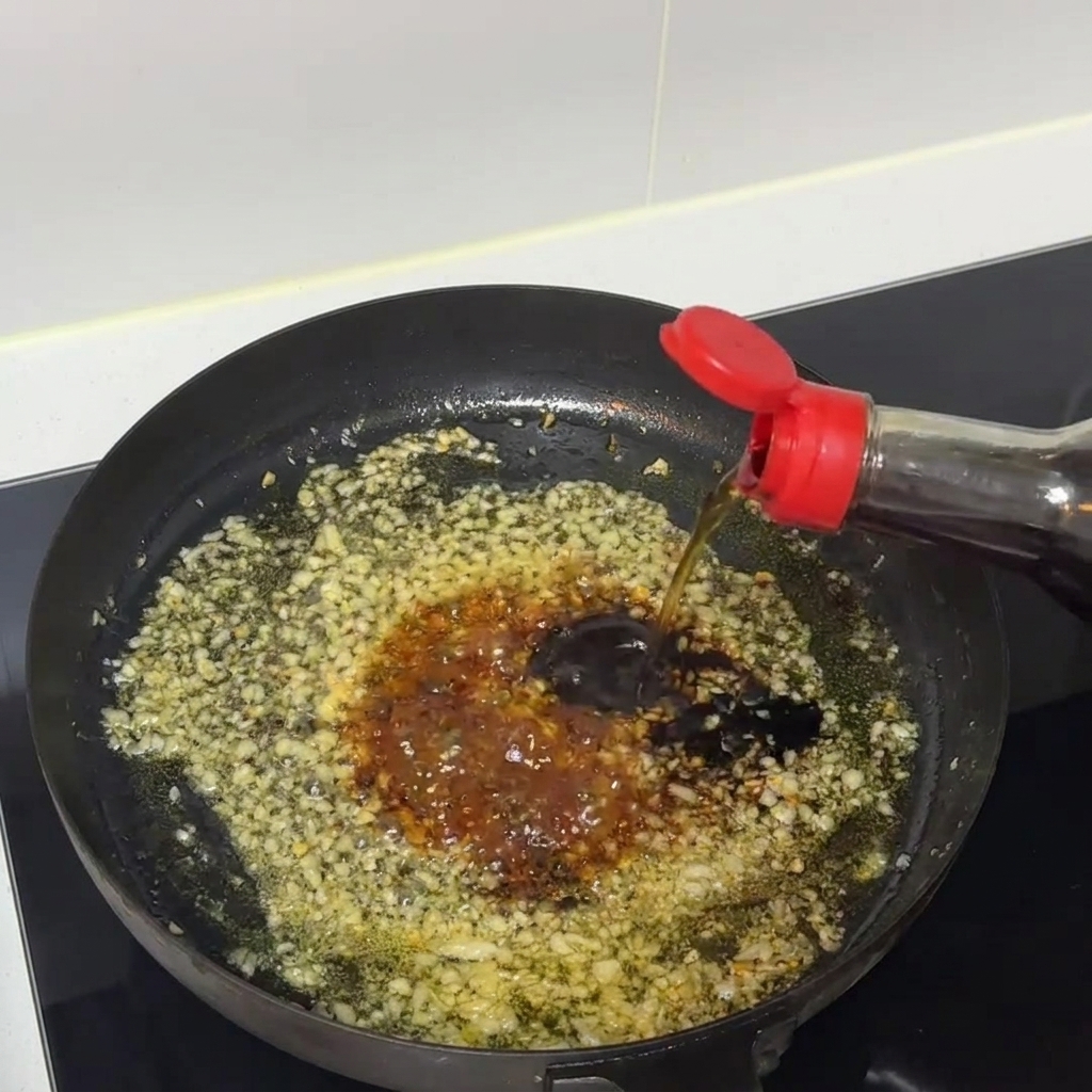 Composto di salsa scura che sobbolle e viene mescolato allinterno di una padella con aglio tritato.