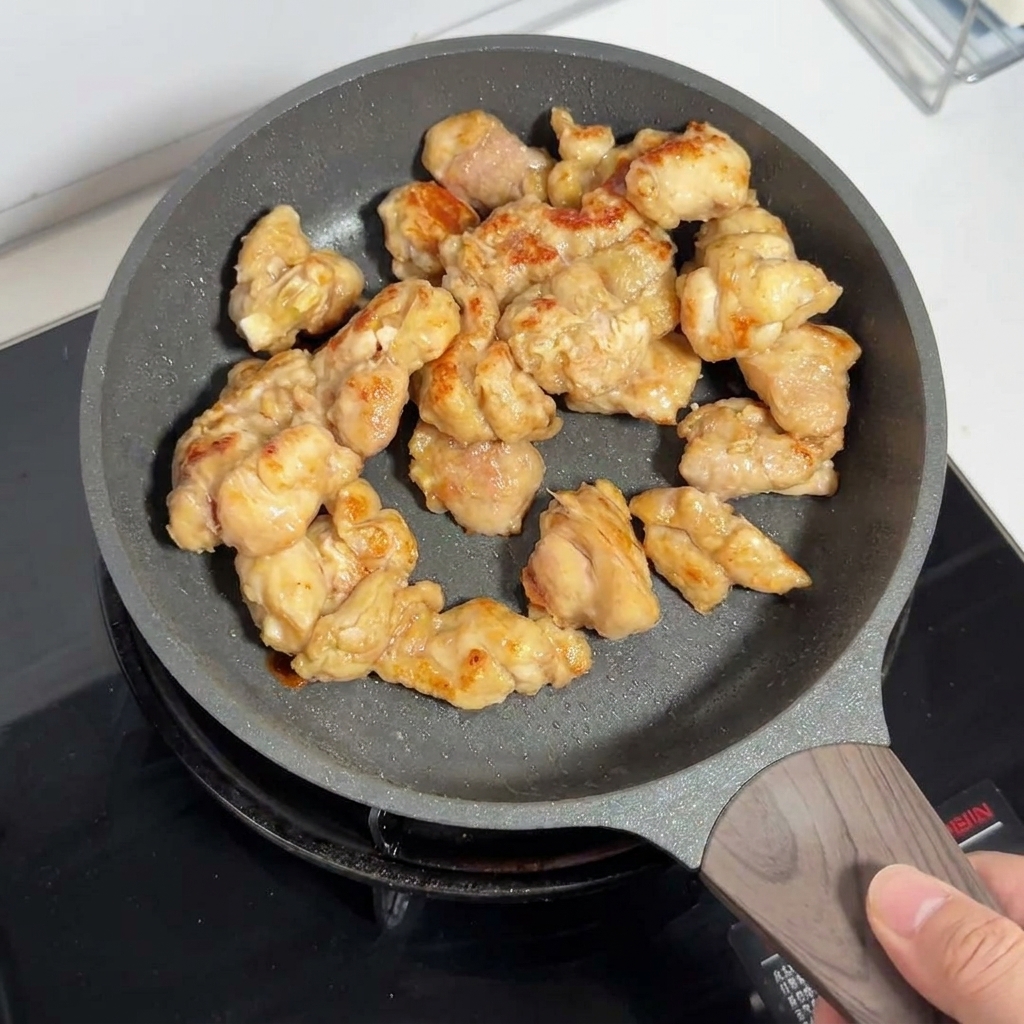 Pezzi di coscia di pollo dorati che cuociono allinterno di una padella antiaderente.
