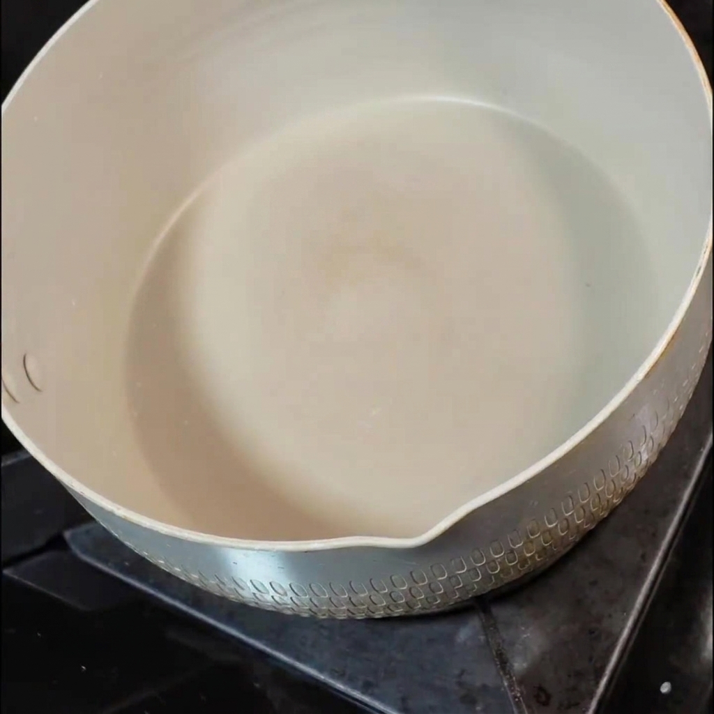 Una piccola noce di burro che si scioglie allinterno di una padella in ceramica bianca su un fuoco della cucina.