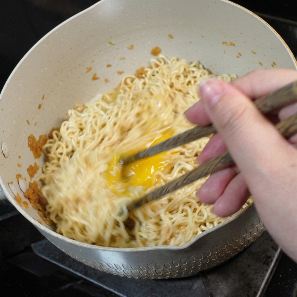 Un uovo mescolato e strapazzato nei noodle allinterno di una padella usando le bacchette di legno.