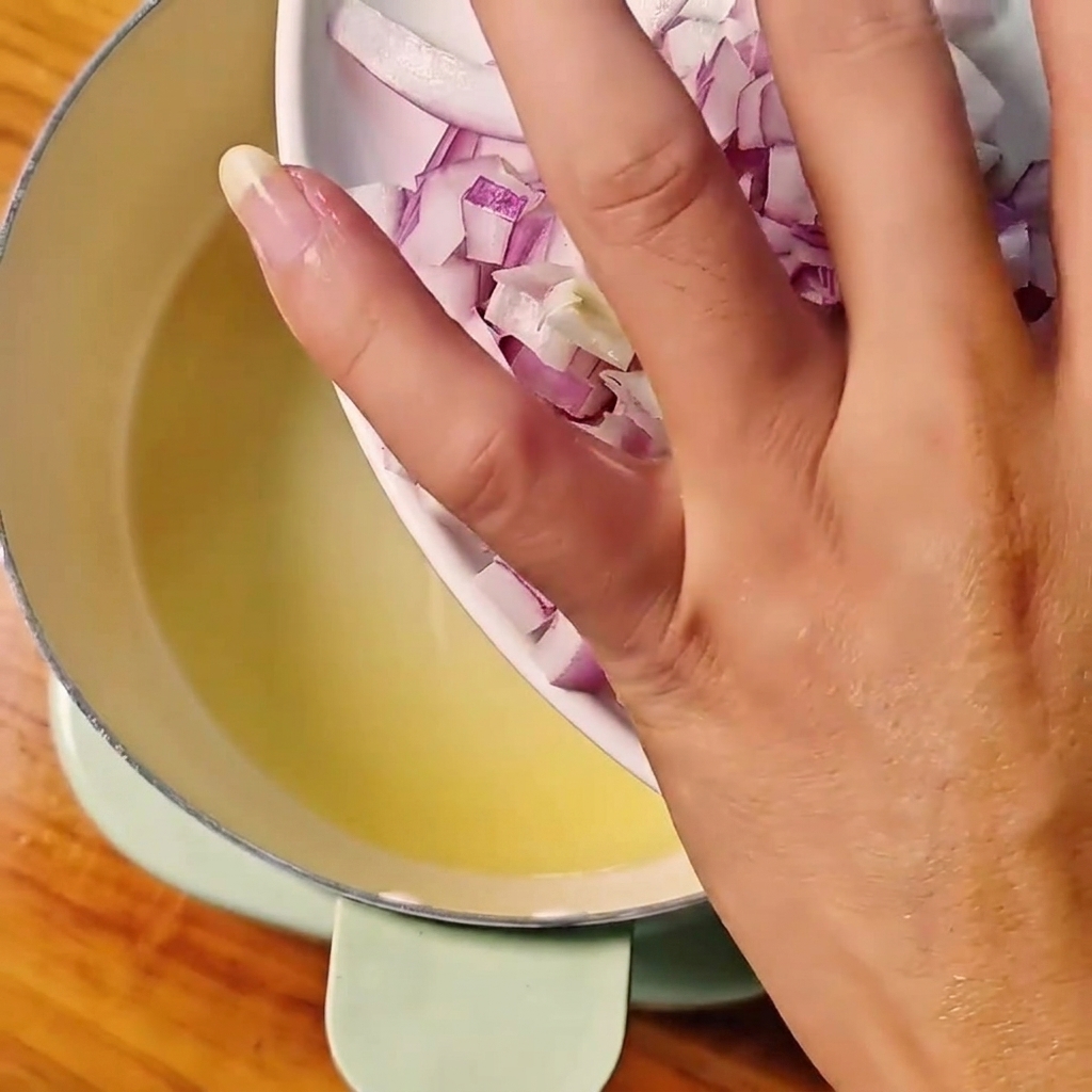 Cipolle rosse a dadini versate da un piatto bianco in una pentola con olio caldo.