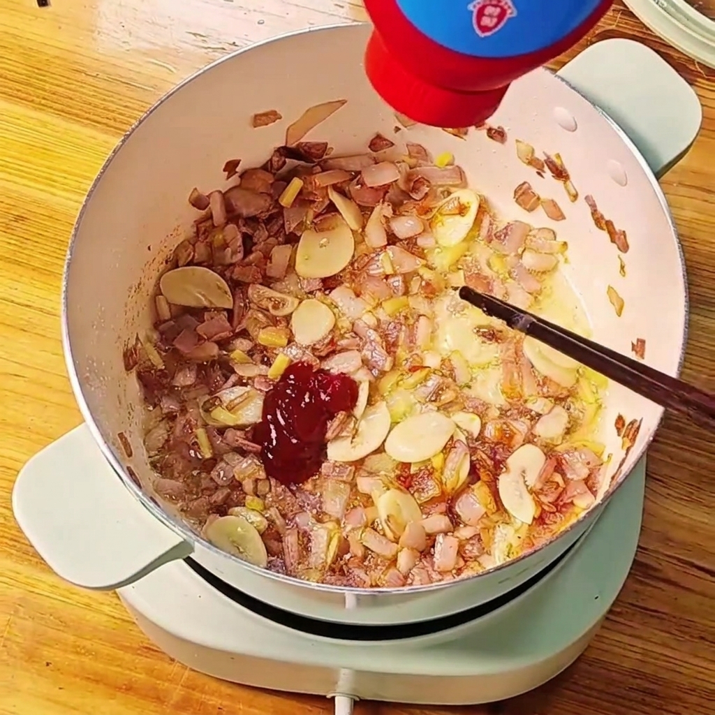 Concentrato di pomodoro rosso spremuto da un tubetto in una pentola di cipolle e aglio soffritti.