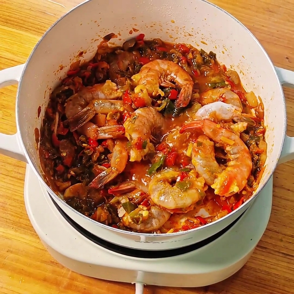 Acqua pulita versata da una ciotola piccola in una padella con gamberi e salsa.