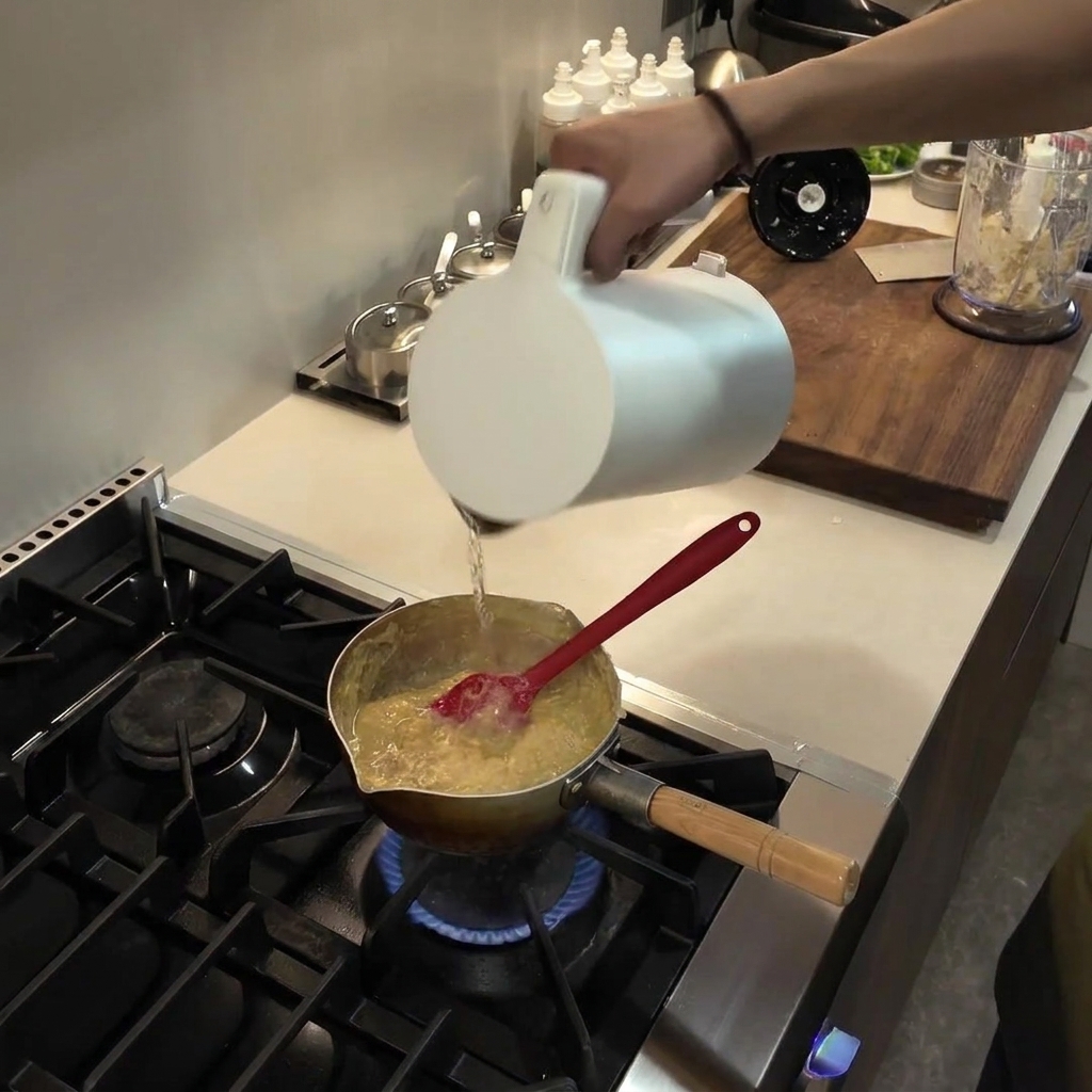 Versamento di acqua da una brocca bianca in un pentolino contenente un composto di fufu denso e in ebollizione.