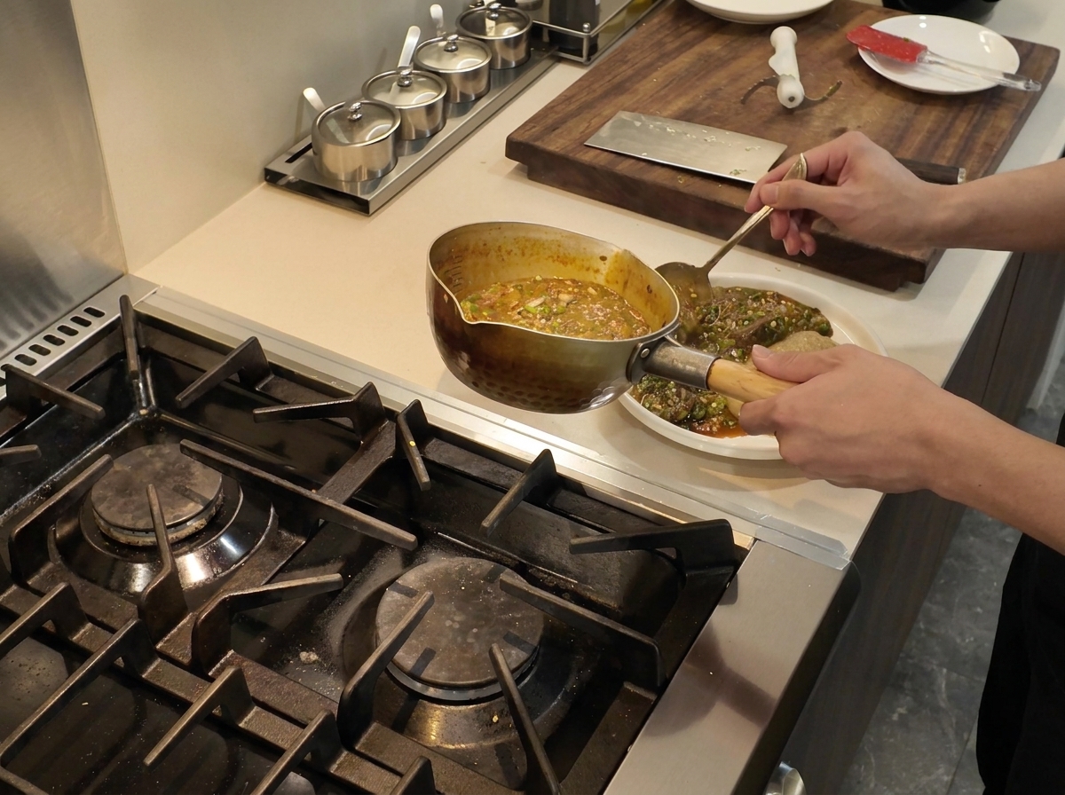 Un meti-mestolo che versa bollente stufato di okra e pesce su un piatto bianco accanto a una porzione quadrata di fufu.
