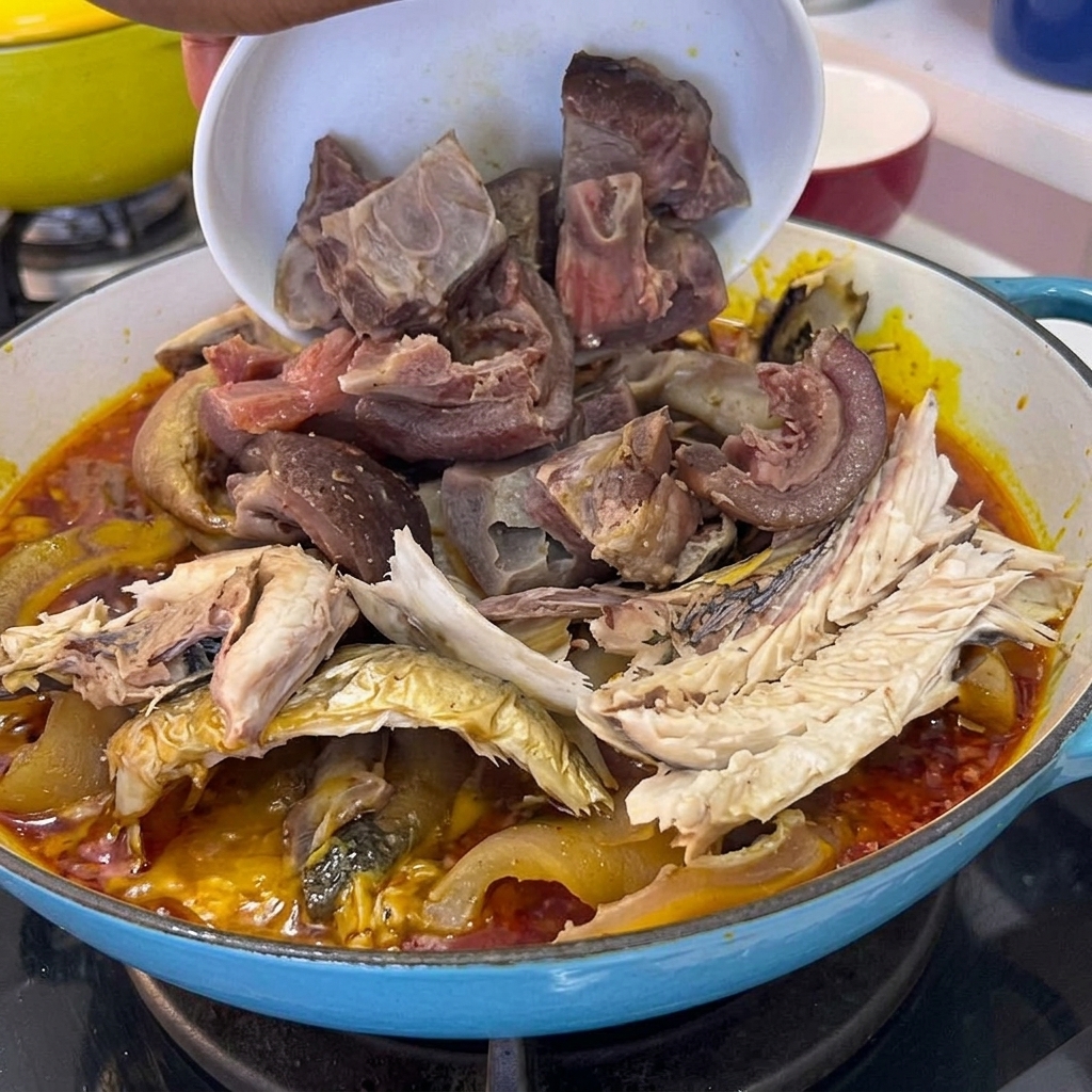 Pezzi di carne di maiale cotta versati da una ciotola nella pentola contenente pesce e salsa.
