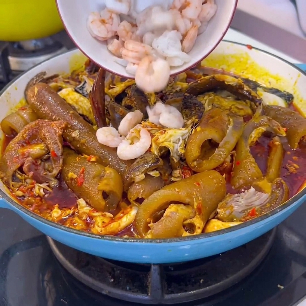 Una ciotola di gamberi bianchi pelati aggiunta in una pentola di cottura piena di cotenna di maiale brasata e salsa di peperoncino.