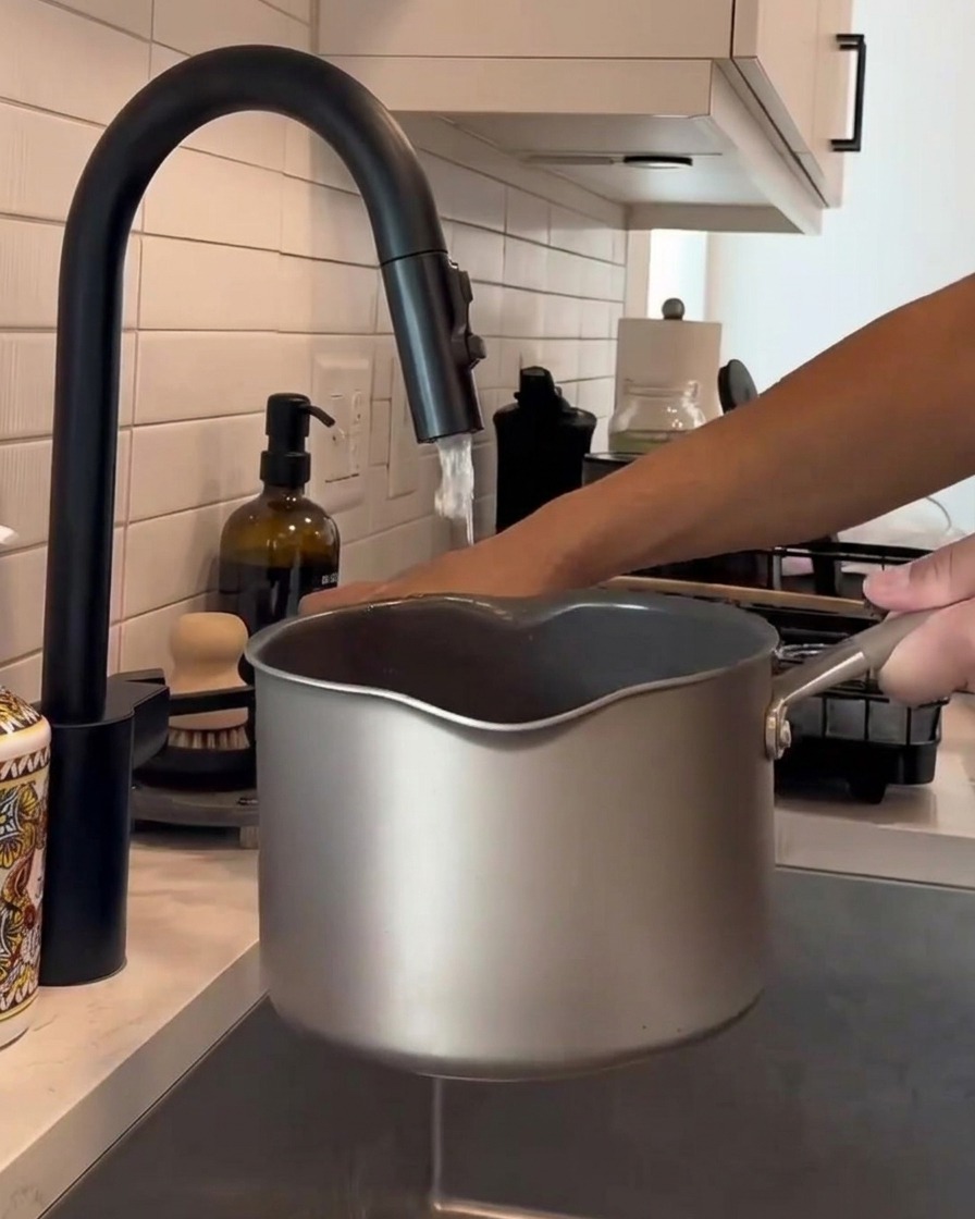 Mani che mescolano il riso bianco dentro una pentola di metallo sotto lacqua corrente del rubinetto della cucina.