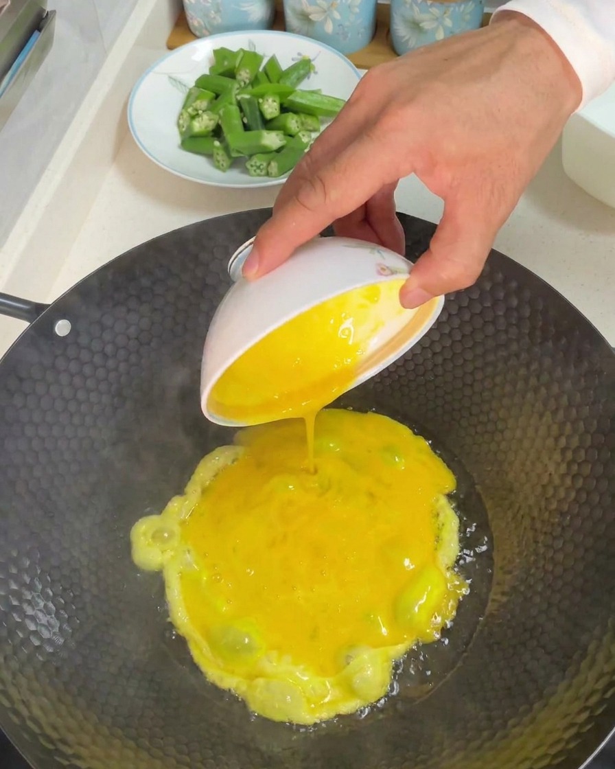 Versare una ciotola di uova gialle sbattute in un wok caldo con olio.