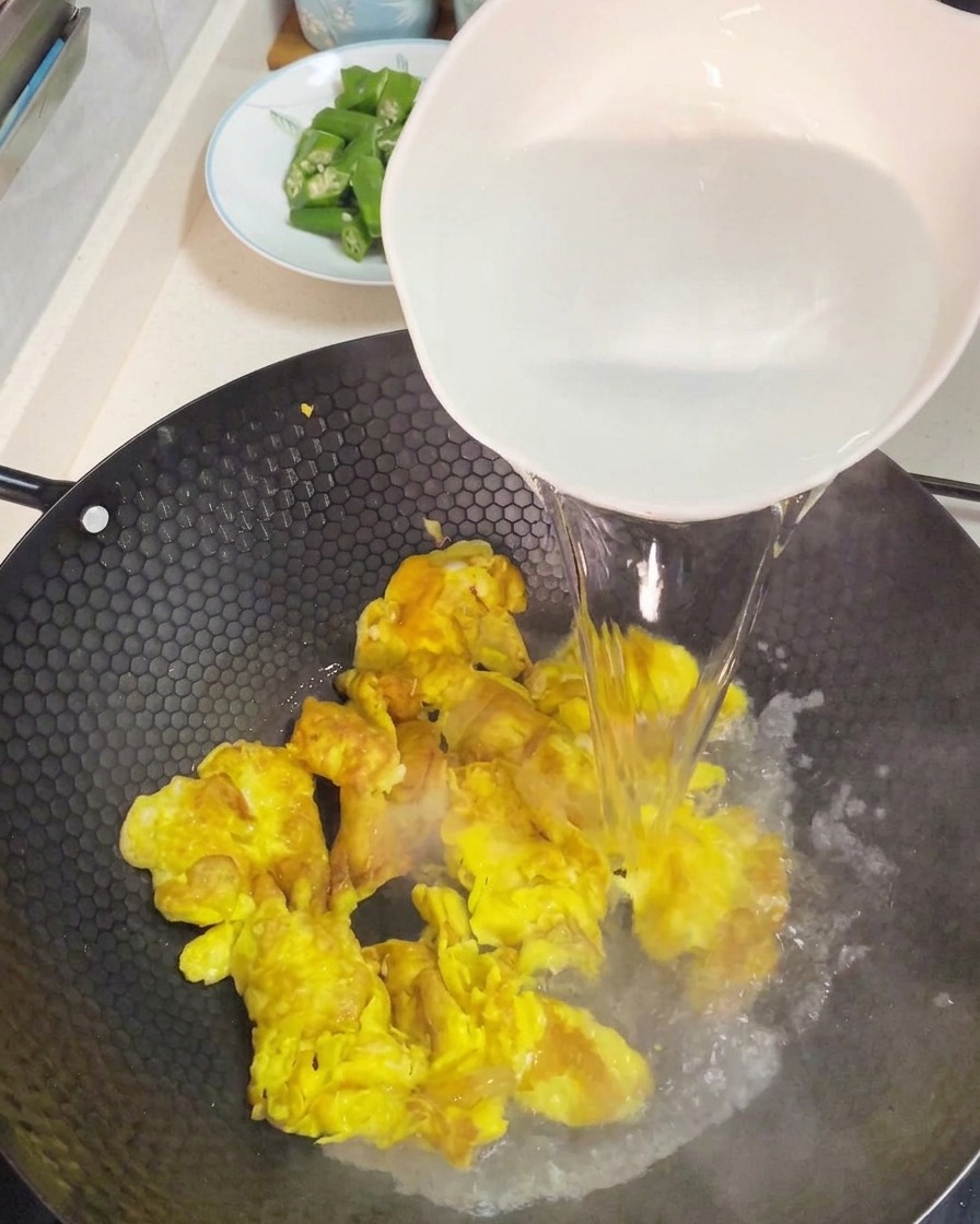 Versare acqua bollente da una grande ciotola bianca sopra le uova strapazzate per creare una base per zuppa.