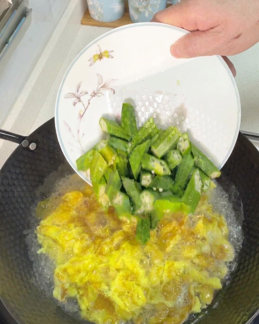 Aggiungere pezzi di okra verde tagliata fresca in un wok di zuppa di uova bollente.