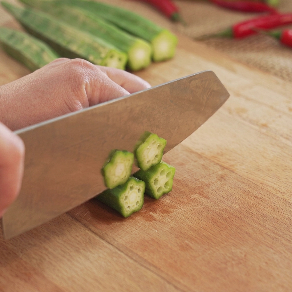 Okra verde tagliata a fette rotonde a forma di stella su un tagliere di legno con un coltello da cucina.