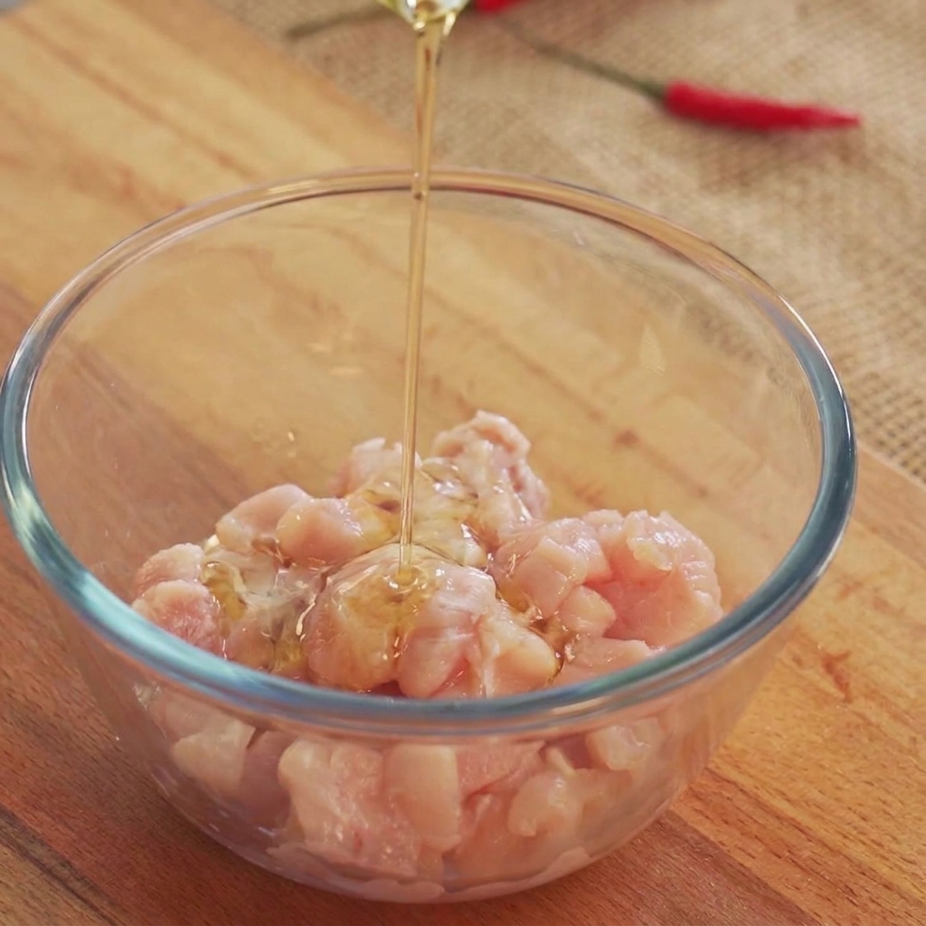 Olio da cucina versato dallalto su pezzi di pollo crudo allinterno di una ciotola di vetro.