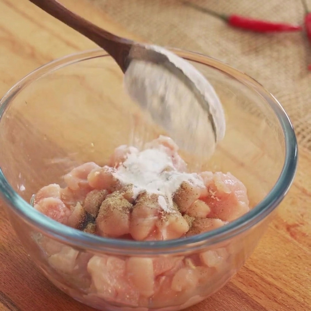 Vino da cucina e condimenti in polvere bianca cosparsi sui cubetti di pollo crudo in una ciotola di vetro.