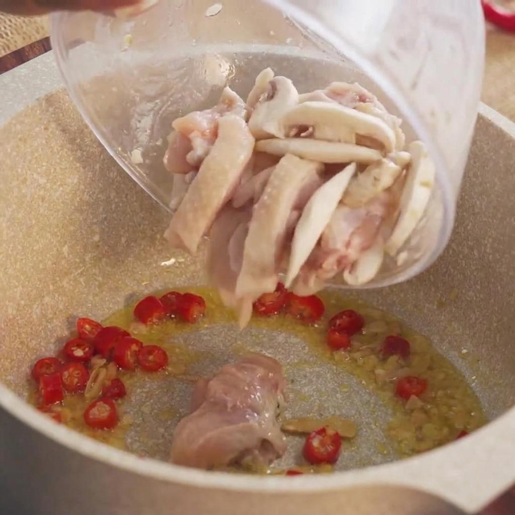 Pezzi marinati di pollo crudo versati da una ciotola nella pentola calda.