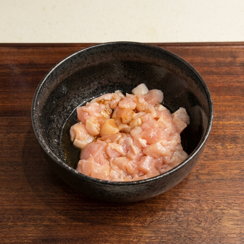 Pollo crudo a cubetti in una ciotola nera con salsa di soia versata sopra.