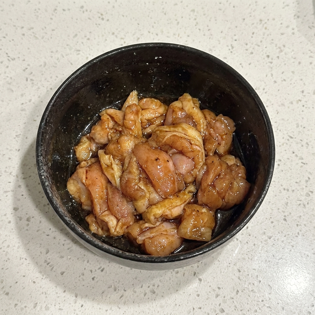 Pezzi di pollo crudo marinati mescolati accuratamente allinterno di una ciotola nera.