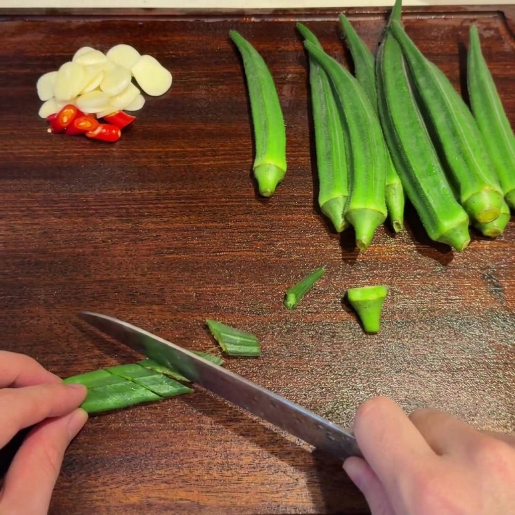 Okra verde sbollentata tagliata diagonalmente con un coltello su un tagliere di legno.