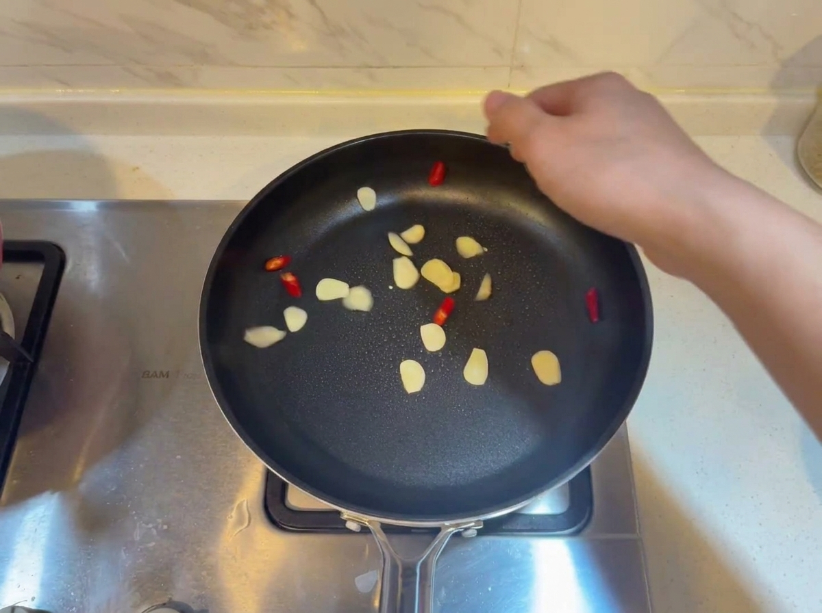 Fette daglio e pezzi di peperoncino rosso che sfrigolano in una padella calda con olio.