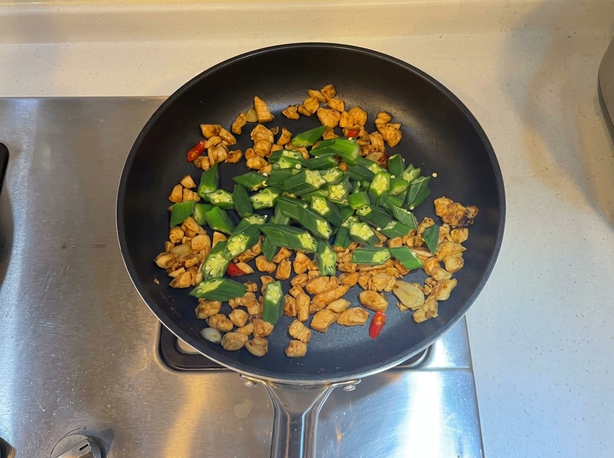 Fette di okra verde mescolate nella padella con il pollo cotto e gli aromi.