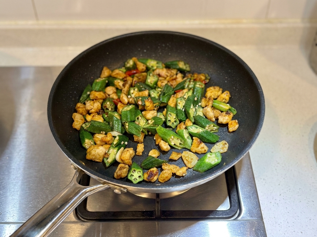 Pollo e okra saltati finiti nella padella, leggermente asciutti e pronti per essere serviti.