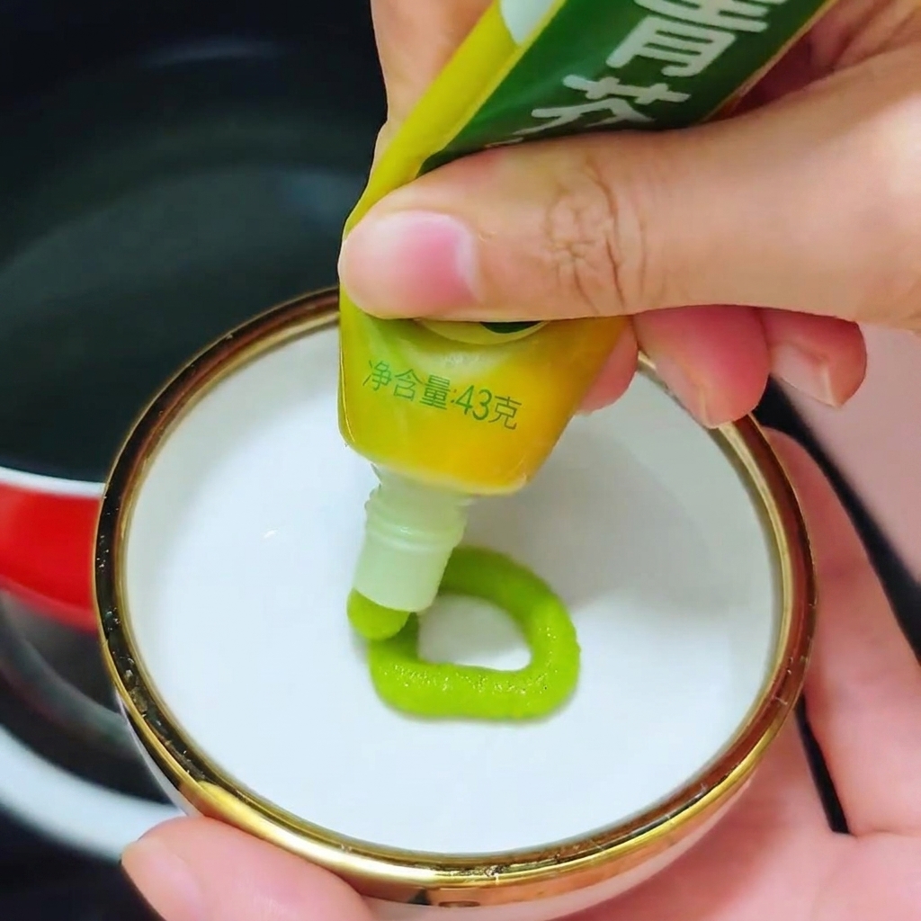 Una persona che spreme un cerchio di pasta di wasabi verde brillante da un tubetto in un piccolo piatto bianco.