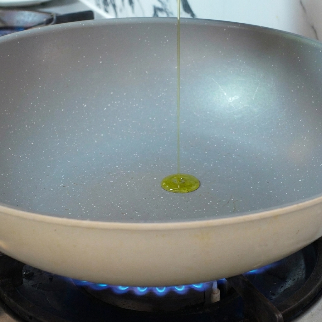 Olio doliva versato in una padella di ceramica preriscaldata sopra una fiamma a gas blu.