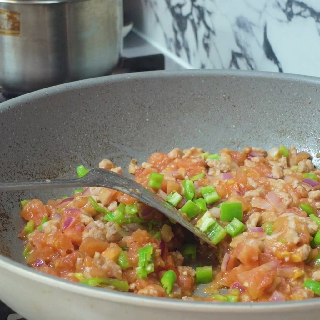 Acqua versata da un contenitore in una padella riempita con un miscuglio di carne macinata e verdure a dadini.