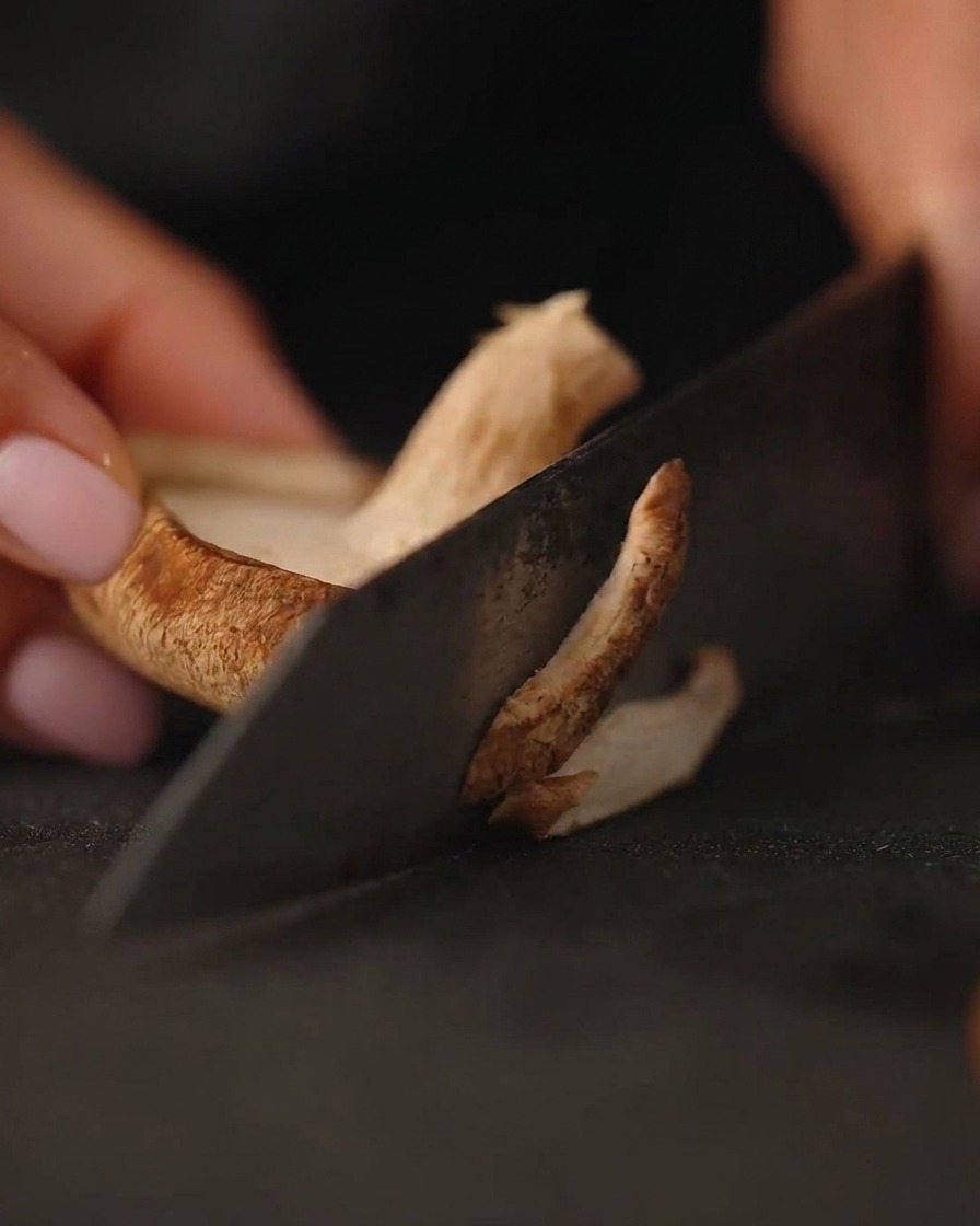Primo piano di funghi freschi tagliati a fette su un tagliere scuro con un coltello.
