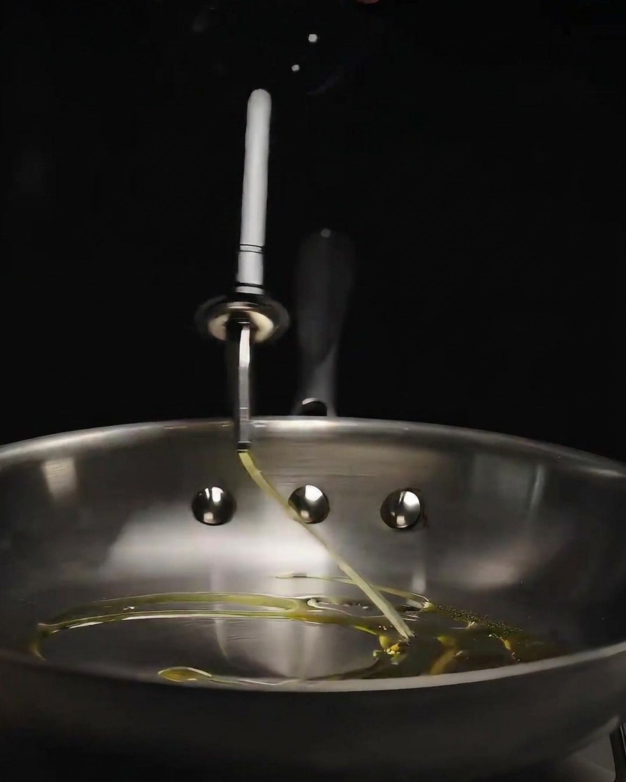 Olio doliva versato da una bottiglia di vetro in una padella di acciaio inossidabile lucida.